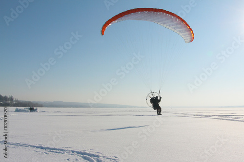 The person flying on a motorized paraplane against the snow 
