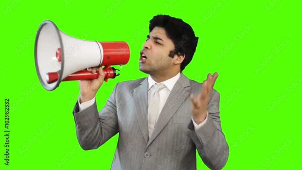 Young businessman talking into a megaphone on green background Young businessman talking into a megaphone on green background