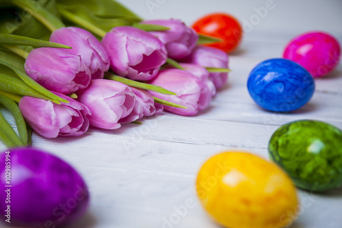 Colorful easter eggs with pink tulips on white wooden table
