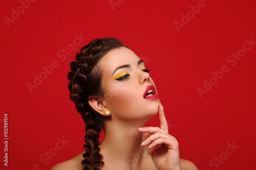 The beauty surprised girl fashion model smiling. Funny braids hairstyle, nails and beige bright makeup, isolated on a red background. Positive emotions smile. Beautiful young woman portrait