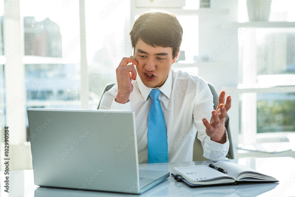 Busy asian businessman working on laptop and calling