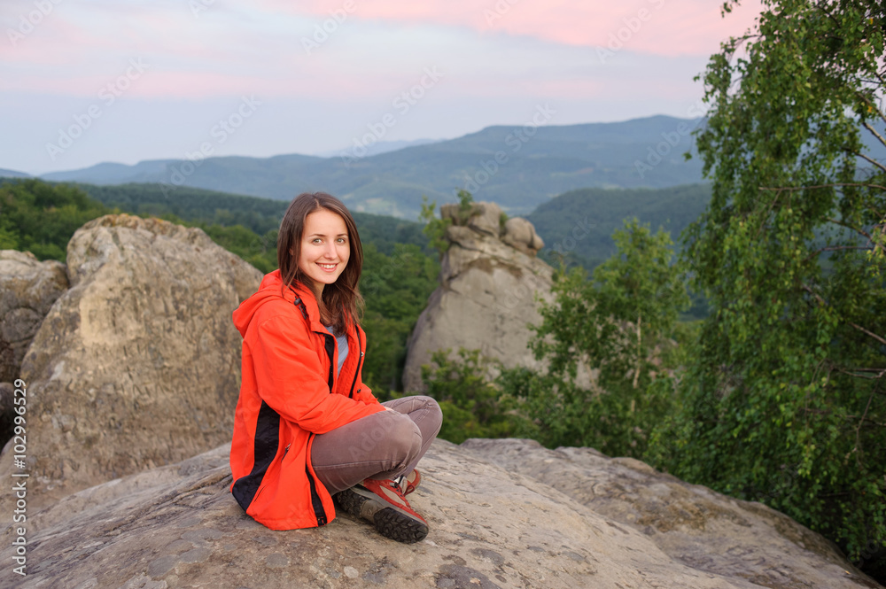 Naklejka premium lady hiker sitting with her leg crossed on big rock on top of th