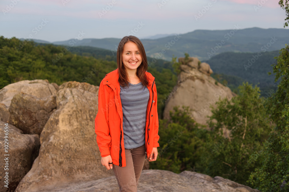 Portrait of young happy female hiker standing on rock on top of