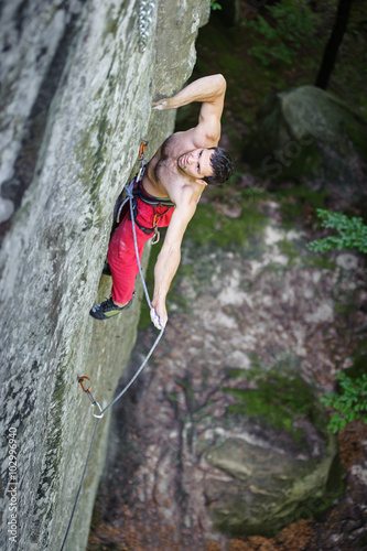 Young athletic man rock-climbing on large boulders with rope eng