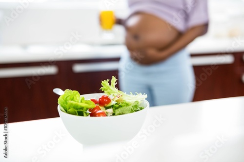 Pregnant woman in kitchen with salad on table 