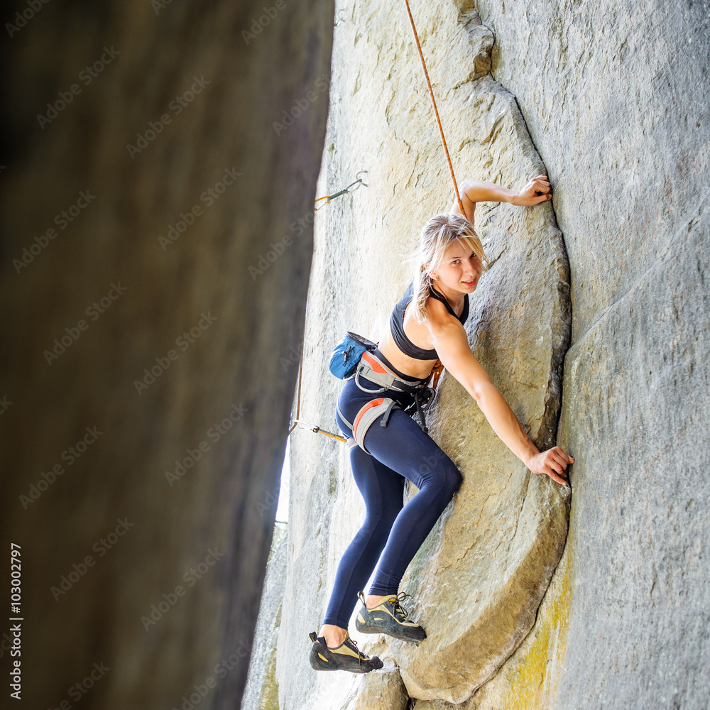Strong pretty woman climbing steep stone wall in nature, with ro - obrazy, fototapety, plakaty 
