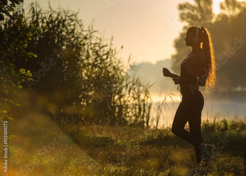 Young attractive female runner in nature with earphones listenin