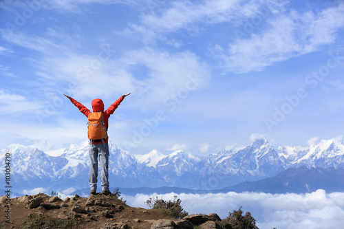 cheering young woman hiker open arms to beautiful snow mountain summits