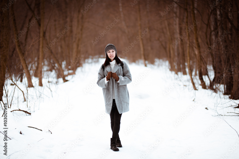 Portrait of a happy beautiful girl with brown hair in  winter forest.Attractive brunette woman dressed in a hipster style with black stylish leather backpack wearing grey coat and white pullover.