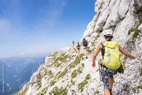 group climbing the mountain, narrow path in the steep slopes of the Alps, blue sky and magnificent views photo