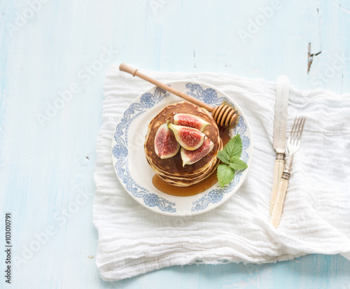 Pancake tower with fresh figs and honey on a rustic plate. Light blue background