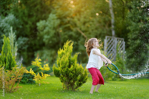 Adorable little girl playing with a garden hose on summer evening