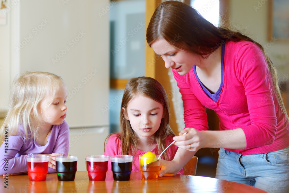 Young mother and her two little daughters painting colorful Easter eggs Young mother and her two little daughters painting colorful Easter eggs