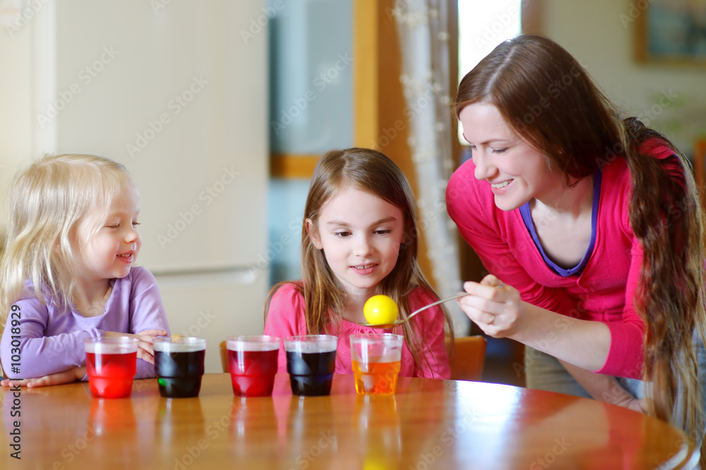 Young mother and her two little daughters painting colorful Easter eggs Young mother and her two little daughters painting colorful Easter eggs