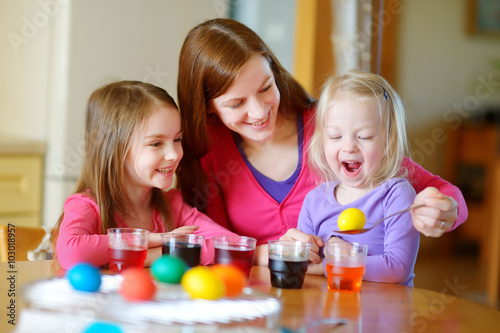 Young mother and her two little daughters painting colorful Easter eggs