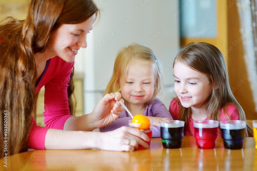 Fototapeta premium Young mother and her two little daughters painting colorful Easter eggs
