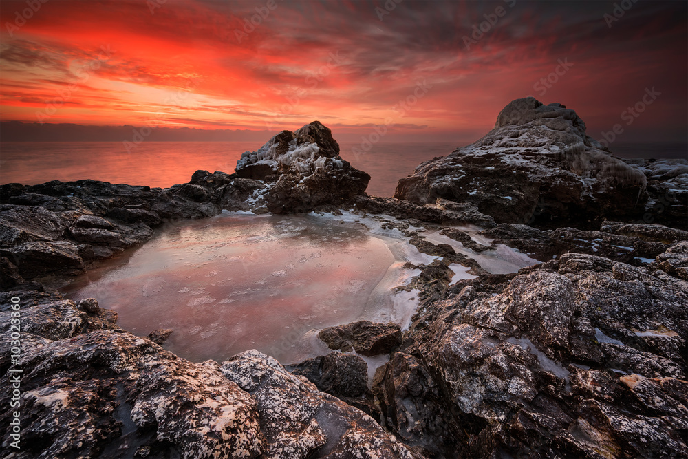 Fototapeta premium Fire and ice. Rocky beach long exposure winter seascape at sunrise, Bulgaria.