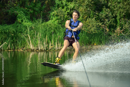 Happy handsome man wakesurfing in a lake