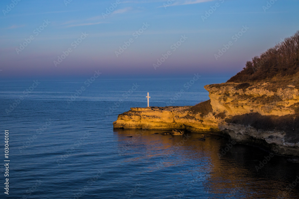 Cross on shore rocks in sunset time