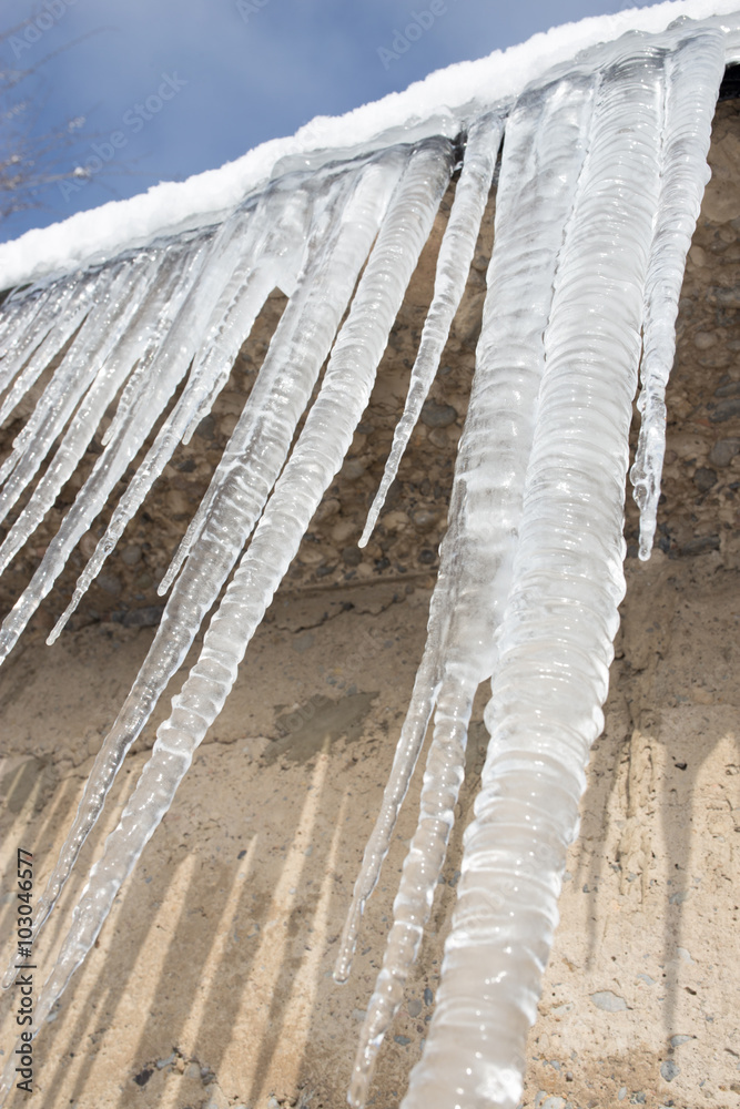 Fototapeta premium Large icicles hanging on the roof of the house in springtime