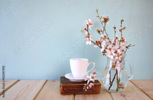 old book, cup of coffee next to spring white flowers on wooden texture
