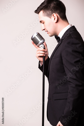 Side portrait of young man in suit singing with the microphone. Isolated on grey background. Singer concept.