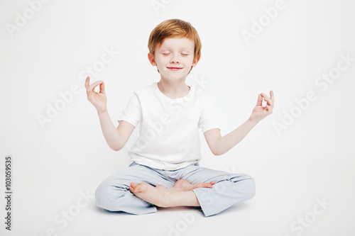 Little cute red-haired boy sitting on a white background in the