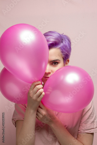 Violet short-haired woman in pink pastel smiling behind balloons