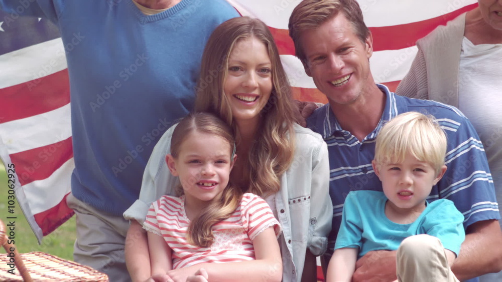 Happy family smiling with an american flag in a park Happy family smiling with an american flag in a park
