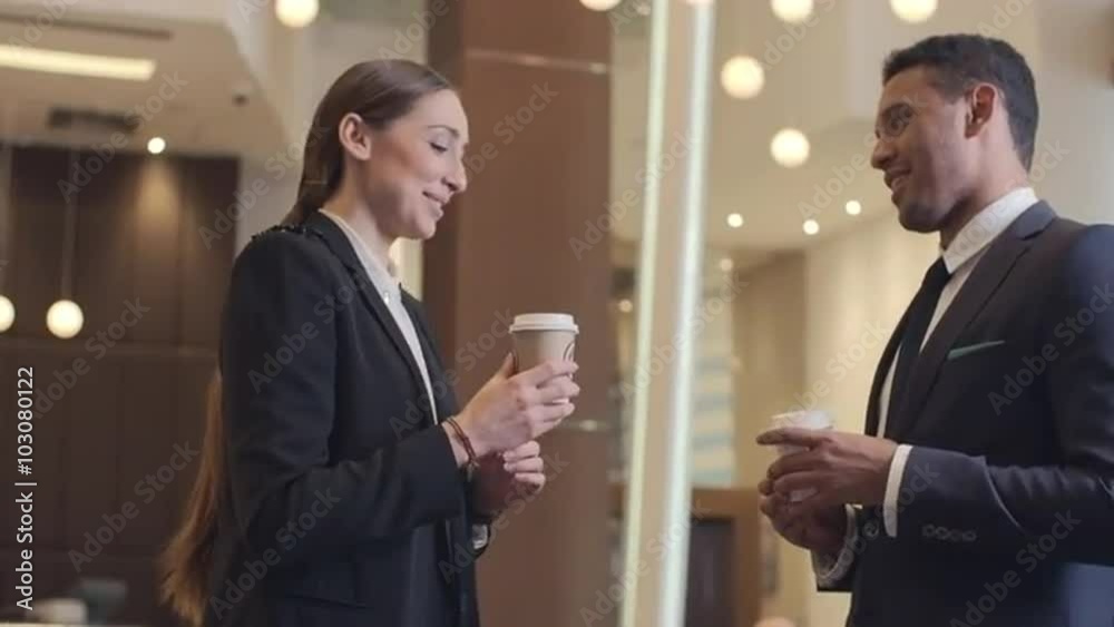 Woman checking the time whiles her colleague coming with two coffee cups and talking