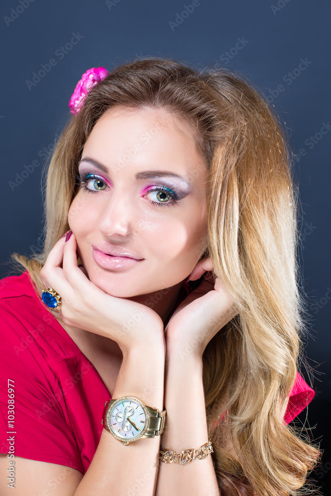 Beautiful blonde girl with bright makeup, long curled hair and massive jewelry on grey background. Fashion shot.