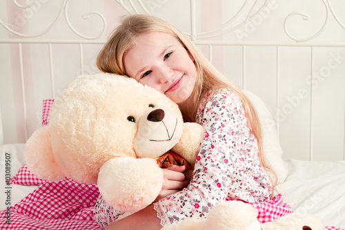 Little girl sitting on bed and hugging teddy bear