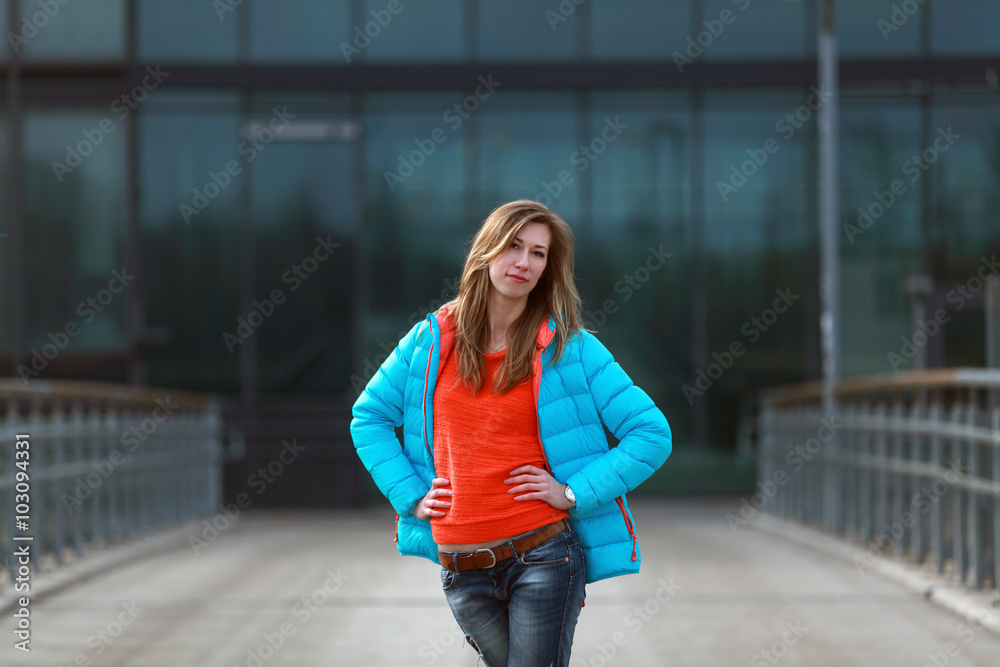 Beautiful blonde woman wearing blue jacket, orange pullover and blue jeans on the street