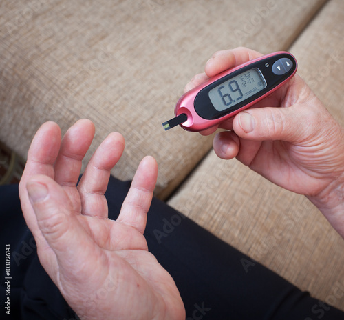 Medicine, diabetes, glycemia, health care and people concept - close up of woman checking blood sugar level by glucometer and test stripe at home