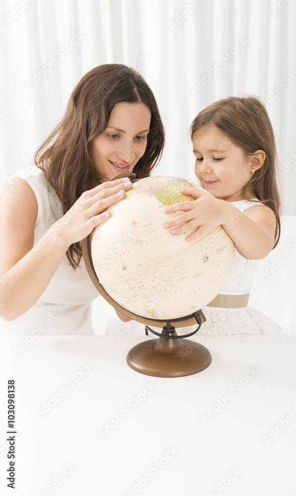 Little girl and her mother looking at a terrestrial globe. Little girl discovering world geography using vintage globe.