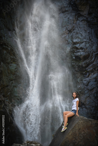 girl on rock with waterfall background © dizitsyn