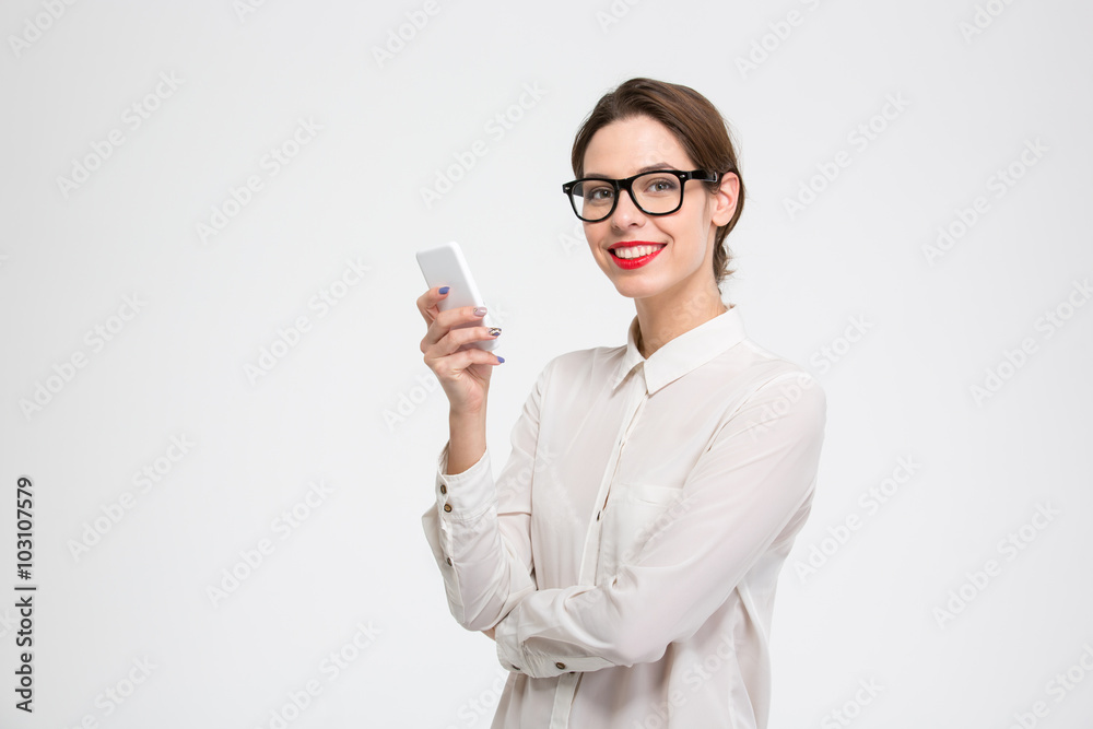 Cheerful attractive businesswoman in glasses standing and using mobile phone Cheerful attractive businesswoman in glasses standing and using mobile phone