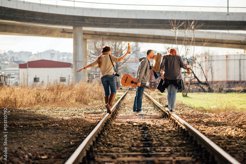 Four happy friends, boys and girls walking with guitar and beer