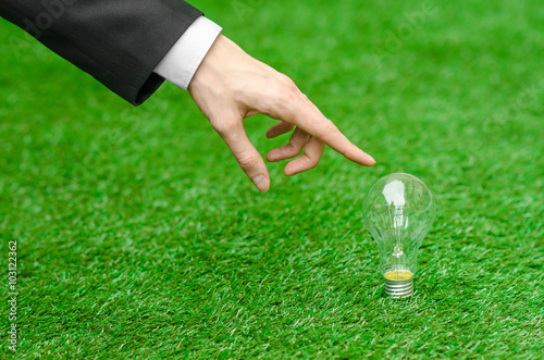 Electricity and business theme: a man in a black suit holding a light bulb against a background of green grass