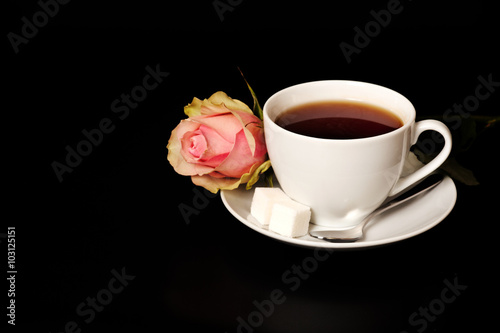 White cup of tea on the black background table with red rose