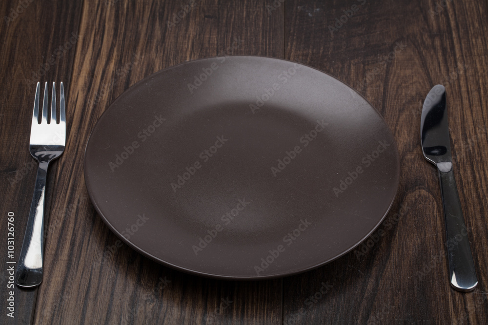 Knife, dark brown plate and fork on wood background Knife, dark brown plate and fork on wood background
