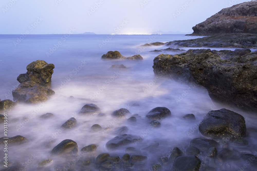 Coastal Glow - Time lapse photograph of atlantic ocean and a rocky shore line with the glow of another island nightlife on the horizon