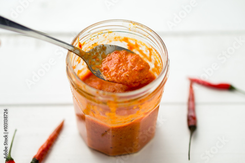 Piri piri sauce is a type of hot chilli pepper sauce used as seasoning or marinade traditionally in portuguese cuisine. Seen here in a glass jar with a spoon, on a white background. photo