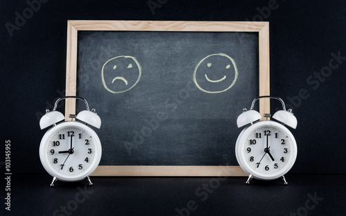 Two vintage alarm clocks showing 9 and 5 o'clock with happy and sad smileys on chalkboard on black background. Nine to five corporate working hours concept. photo