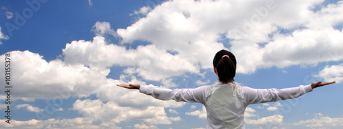 Woman with arms outstretched against the sky with clouds