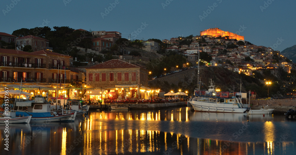People eating in harbor side restaurants in the early evening, castle and quayside illuminated.