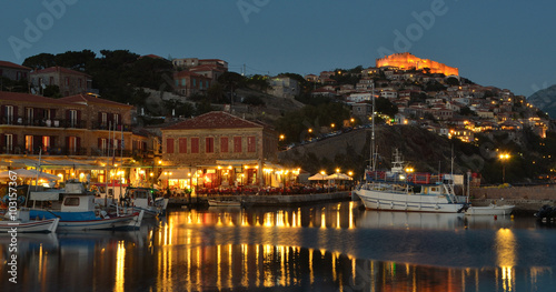 People eating in harbor side restaurants in the early evening, castle and quayside illuminated.