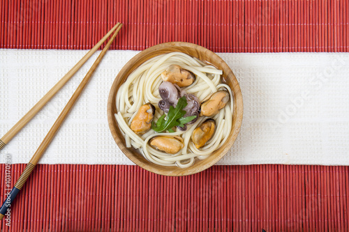 Fotografija Noodles with mussels and octopus in wooden plate on a red makisu