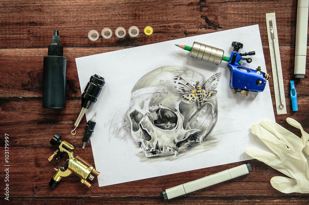 skull tattoo sketch with rotary machines, needles, grips on wooden background