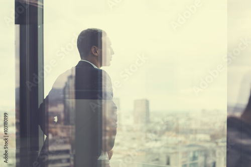 Business man looking out through the office balcony seen through glass doors. Post processed with vintage filter.